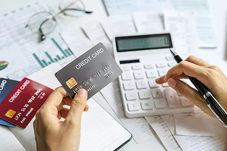 A pair of hands. One hand is holding a credit card/ The other hand is using calculator, calculating finances, likely related to division of debts.