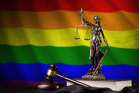 LGBT community flag with statue of lady justice, constitution and judge hammer on black drapery.