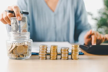 Hand places coin into saving jar, representing how smart finance, and investment, banking practices turn money into financial wealth