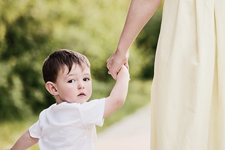 Child boy looks back with fear in his eyes, clutching the woman's hand tightly.