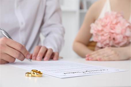 Newlyweds signing marriage contract and wedding rings on desk.