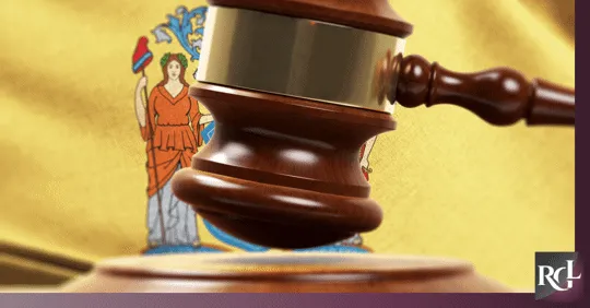 A judge’s wooden gavel in front of a yellow flag featuring the New Jersey state emblem.