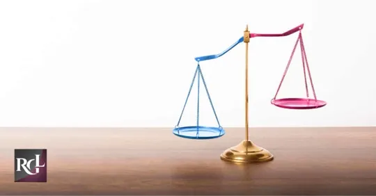 A justice scale with one side colored blue and the other pink, placed on a wooden table with a white background.
