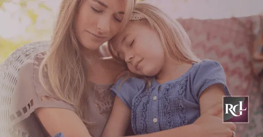 An image of a mother and her little girl sleeping while sitting, with their heads resting against each other.