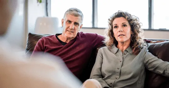 A couple sitting next to each other while talking to someone in front of them.