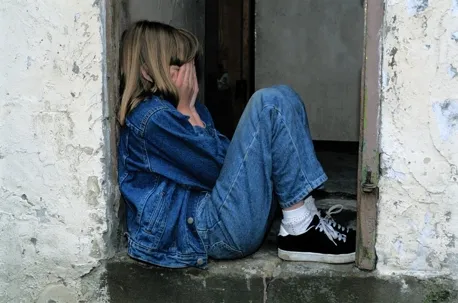 A child is outside the door, curled up and covering their face, as if crying.