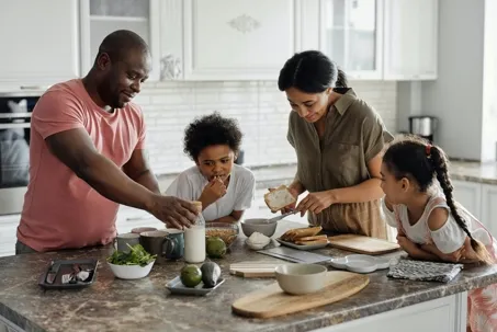 A family is having a meal, with the father and mother preparing food for their kids.