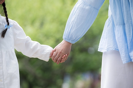 A parent and a child, holding each other outdoors.