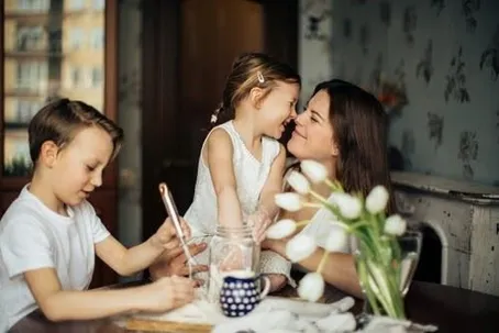 An image of a mother bonding with her two kids, where the mother and daughter are playfully teasing each other.