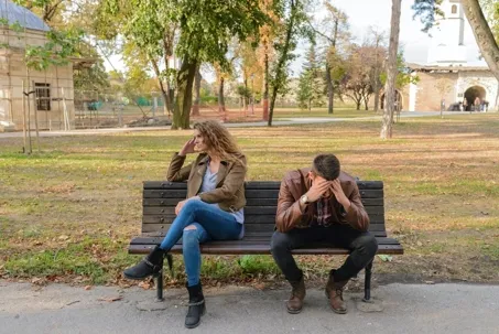 An image of a boy and a girl sitting on a bench, seemingly arguing.