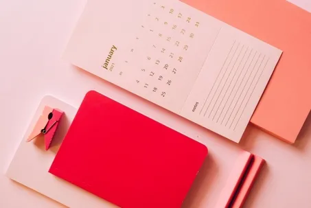 A red notebook, some documents, and a calendar are on the table.