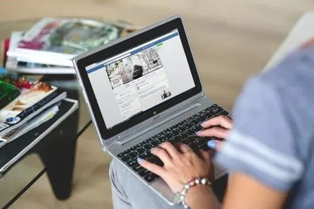 A girl is sitting and using a laptop to search, with many items in front of her.