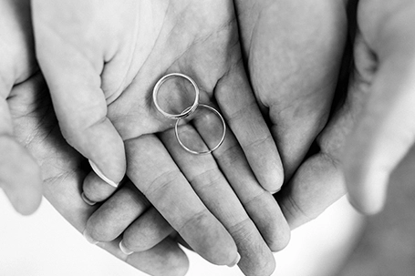 The bride and groom held hands with wedding rings.