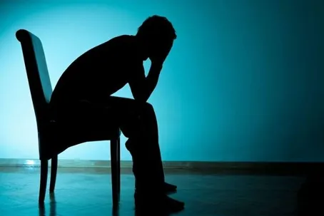 A man sitting on a chair in a dark corner, looking like he has a serious problem.