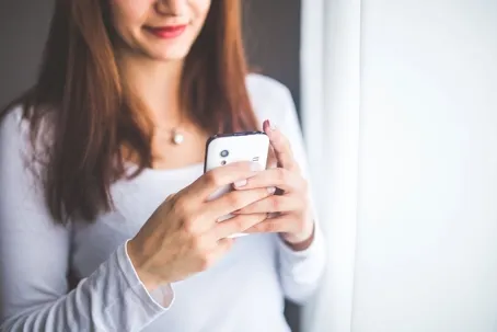 A girl wearing a white long-sleeve shirt and using a white smartphone.