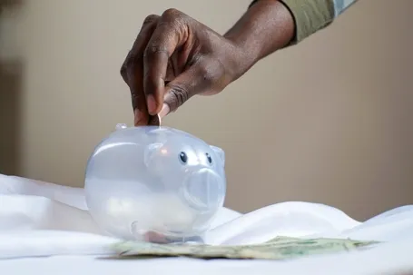 A transparent piggy bank being filled with coins.