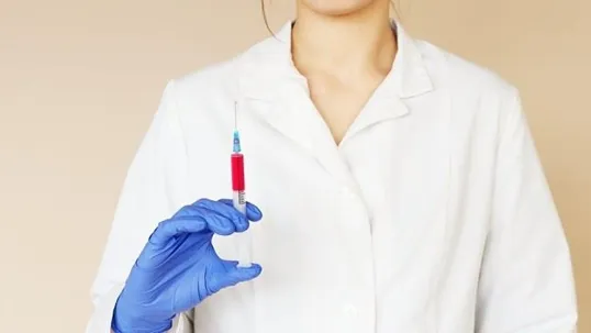 A doctor holding a syringe in his hand while wearing blue gloves.