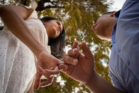 A low-angle shot of a man and a woman holding hands while looking at each other outdoors.
