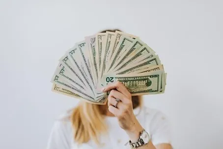 A girl holding a lot of money covering her face.