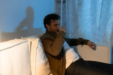 A man sitting alone on the couch while drinking wine.