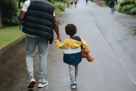 A man walking while holding his son, with their backs turned.