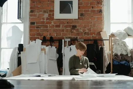 A person sitting at a worktable reviewing papers in a room with fabric patterns and sewing materials.