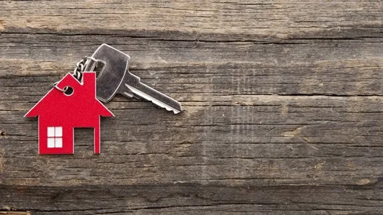 A house key with a red house-shaped keychain placed on a wooden surface.