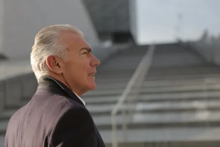 An old man with white hair looking up at a long staircase in front of him.
