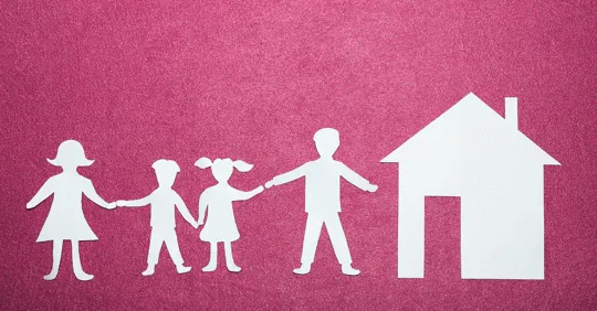 Paper cutouts of a family holding hands beside a house shape on a pink background.