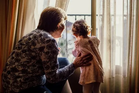 A grandmother and her granddaughter looking out the window.