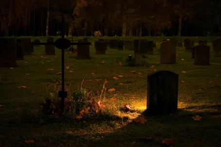 A dark cemetery with only one lit lantern visible.