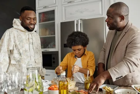 An image of two men with a little boy standing between them, busy preparing food together.
