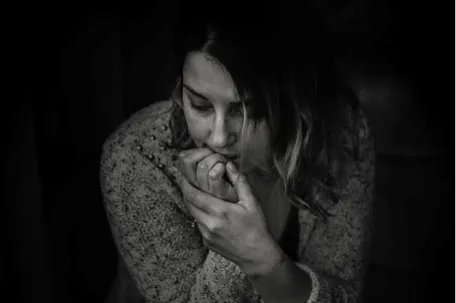 A woman biting her nails, looking down, feeling lonely and stressed against a dark background.