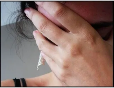 A woman bending forward, using one hand to hold her forehead, partially covering her face.