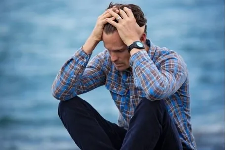 An image of a man holding his hair, feeling stressed and lonely.