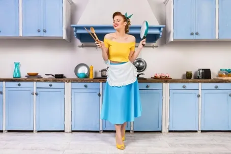 In the kitchen, a woman is holding a kitchen utensil and looking happy.