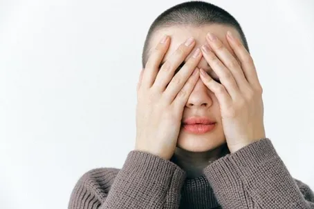 A woman covers her face with her hands against a white background.
