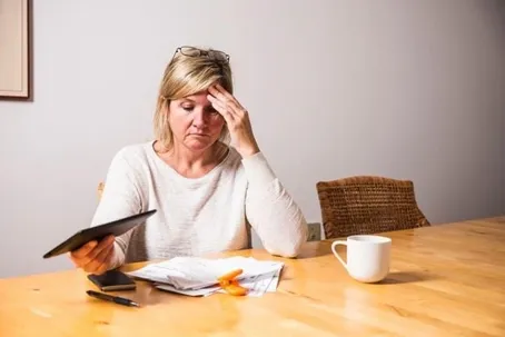 A woman feeling upset while reading a document, with a cup on the table.