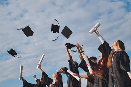 Graduating students hands throwing graduation caps in the air.