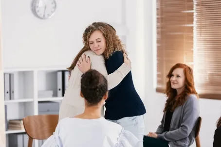 An image of four women, two sitting and the other two hugging.