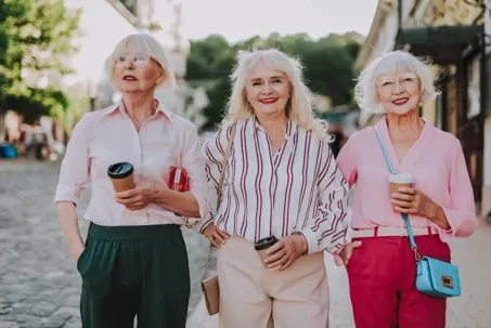 An image of three older women with white hair, smiling while holding cups of coffee.