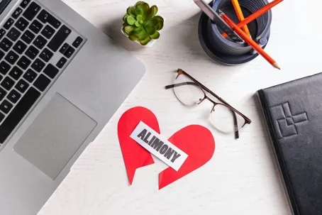 A laptop, a pair of eyeglasses, a flower, and a pen on the table.