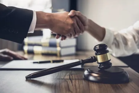 A lawyer and a client shaking hands, with a gavel and books on the table.