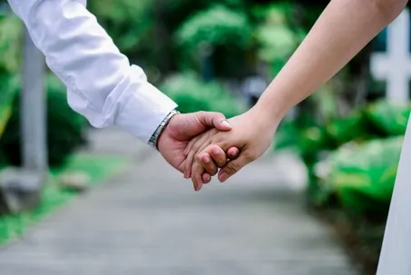 A prenuptial photo showing a close-up of two hands gently holding each other.