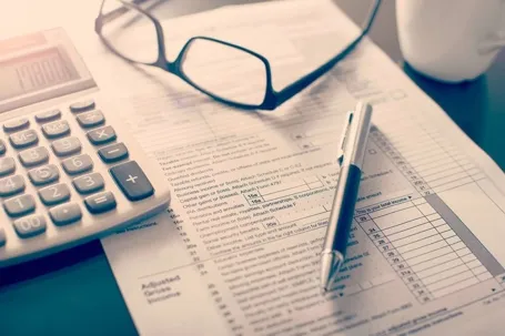 An image of a calculator, sunglasses, a pen, and a paper document.