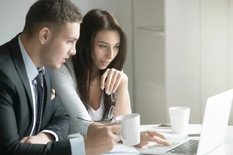 A man and a woman are having a sincere conversation over coffee while looking at a computer.