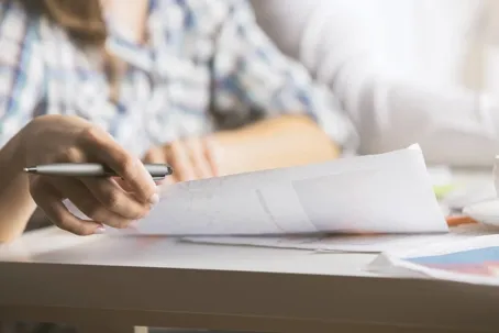 A man holding a pen while flipping through documents on the table in a blurry image.