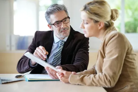 A man and a woman are discussing the paper they have, with the man pointing at it as he explains.