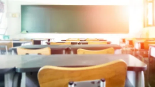 An image of a classroom with chairs, tables, and a greenboard.