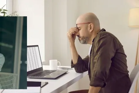 A man looking troubled, massaging his head while facing his laptop.